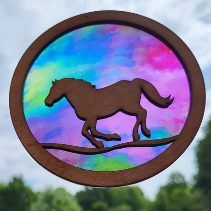 Circular, wooden suncatcher with a horse running. Transparent acrylic background with multi colored rainbow colors. 
