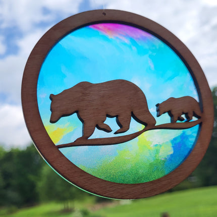 circle suncatcher with wooden foreground of 2 bears walking. Transparent acrylic background of various rainbow colors