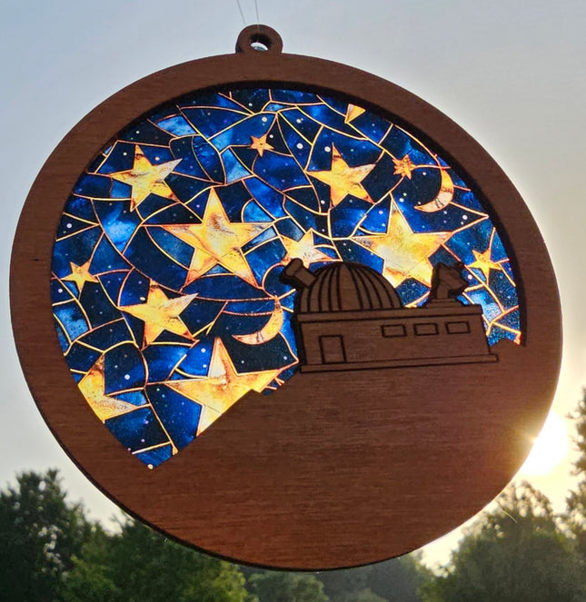 image of a wooden suncatcher in the shape of a circle with an observatory laser etched on a hill. the transparent acrylic background depicts stained glass stars on a night sky