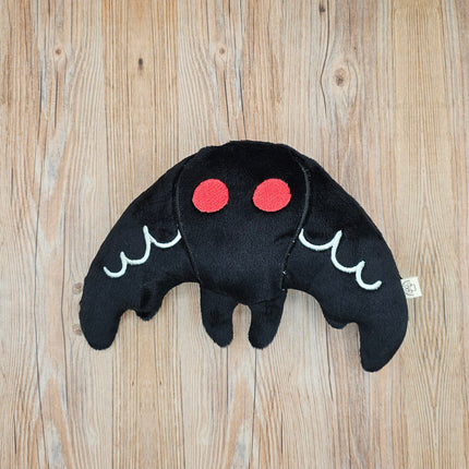 Black plush mothman toy with red eyes and white accents on the wings. 