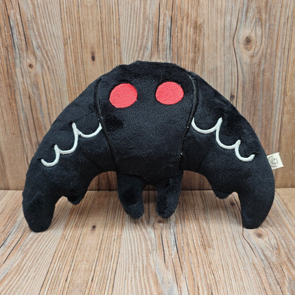 Black plush mothman toy with red eyes and white accents on the wings. 