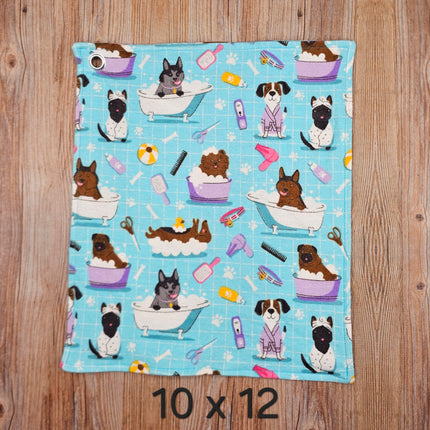 image of a 10x12 flannel towel with dogs in the bath and grooming supplies  on a light blue background. It has  metal grommet in the corner for hanging