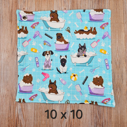 image of a 10x10 flannel towel with dogs in the bath and grooming supplies  on a light blue background. It has  metal grommet in the corner for hanging