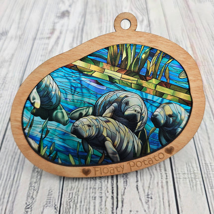 Transparent acrylic "Stained glass" manatee scene in a wooden frame with 'Floaty Potato' laser etched at the bottom. Picture shows close up of suncatcher without light behind it