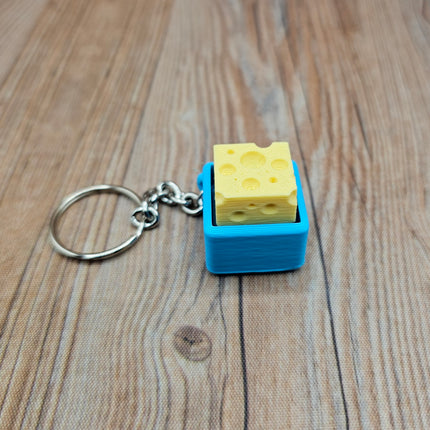 Keychain with a small block of cheese in a blue container on a wooden surface