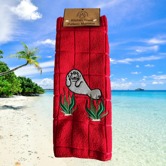 image of a red embroidered polyester kitchen towel. The towel has a cute manatee on the front amongst seaweed