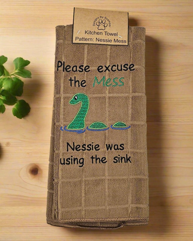 100% polyester, light brown, kitchen towel. Embroidered loch Ness monster with the words, "Please excuse the Mess. Nessie was using the sink."