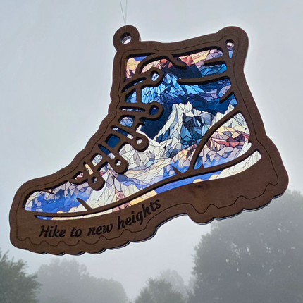 Wooden suncatcher in the shape of a hiking boot with "Hike to new heights" laser etched on bottom of boot. Transparent acrylic background with icy mountains