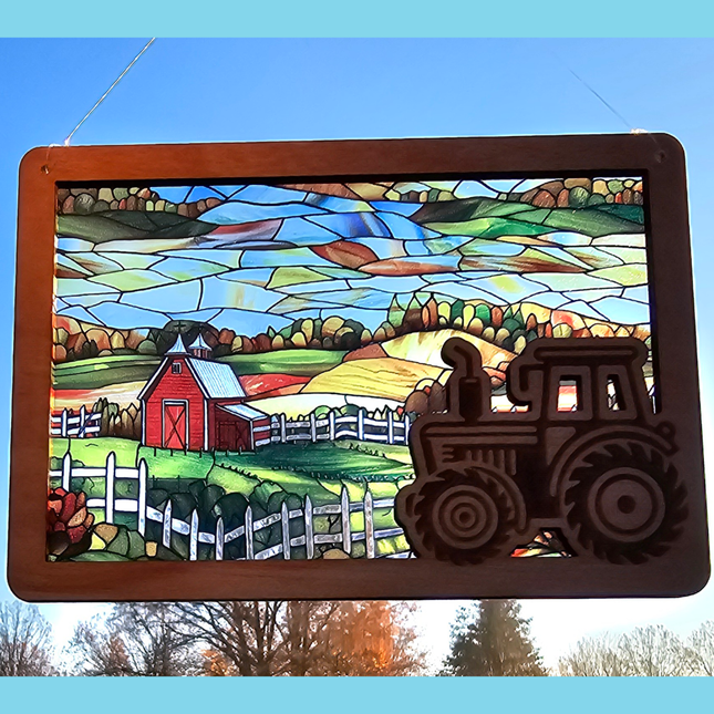 A rectangular suncatcher with a clear acrylic background showing a scenic autumn landscape with a farm tractor in the lower right corner, framed by a wooden border.