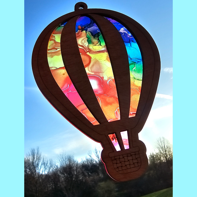 an image of a wooden suncatcher in the shape of a hot air balloon. The transparent acrylic background shows a variety of swirly rainbow colors