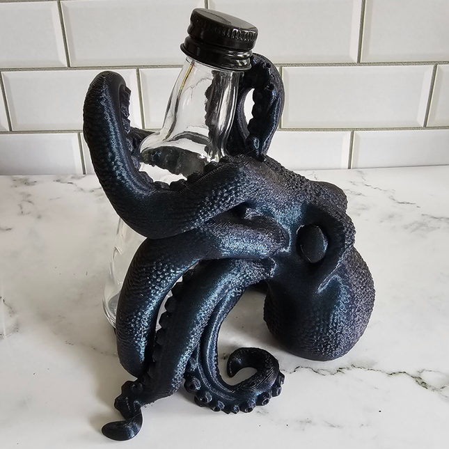 image of a small 3d printed octopus hot sauce holder in the "Burnt Titanium" color option. The octopus is holding a small, empty bottle that comes with the purchase