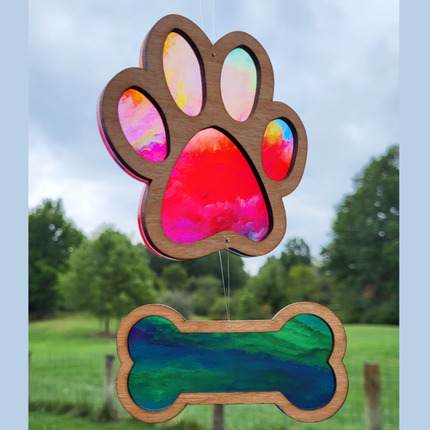 image of a wooden suncatcher with a transparent acrylic background. The top suncatcher is in the shape of a paw and there is a smaller suncatcher in the shape of a bone hanging beneath it. This variety is called "Rainbow Storm"