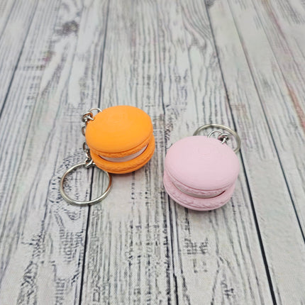 Two macaron-shaped keychains, one orange and one pink, on a wooden surface.